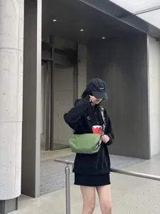 Stylish waterproof green crossbody bag with wide logo strap, paired with casual street style outfit.