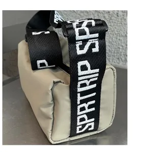 Detail shot of a waterproof coated cylindrical shoulder bag with wide letter-printed strap.
