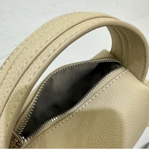 Close-up view of a stylish beige leather lunchbox handbag showing fine stitching and metal zipper.