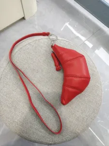 Red soft leather croissant bag, stylish crescent coin purse with long strap and metal hardware.