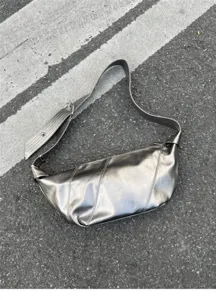 Close-up of metallic silver oil-wax leather shoulder bag with wide strap and chic croissant shape.