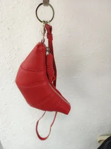 Detail view of the red leather croissant bag hanging on wall hook, showing texture and zipper.