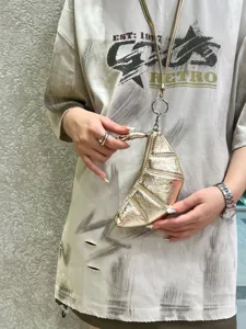 Close-up detail of metallic gold croissant dumpling bag with strap, held in hand.