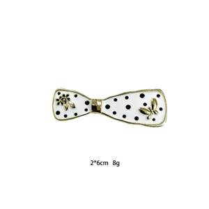 Close-up detail of white bow hair clip with black polka dots, gold edges and floral charms.