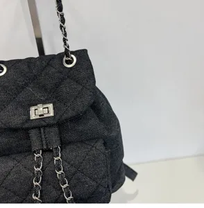 Black denim quilted chain backpack detail, classic diamond pattern with metal strap lock.
