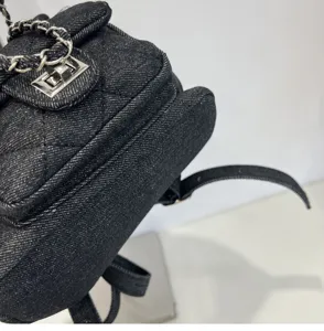 Detailed shot of a black denim quilted backpack with metal chain strap and turn lock.