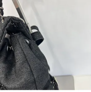 Close-up detail of the black denim chain backpack showcasing metal hardware and texture.