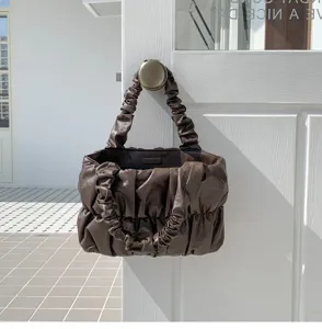 Detail shot of a dark brown ruched cloud handbag hanging on a white door knob, soft leather.