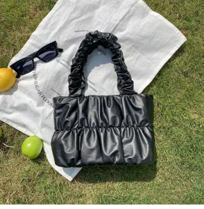 Detailed shot of black pleated cloud handbag on outdoor grass with chic props and sunglasses.