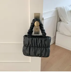 Black pleated cloud handbag detail view, soft PU leather handle design hanging on a door.