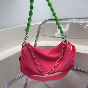 Trendy pink fabric shoulder bag with unique green knotted strap and stylish chain decoration.