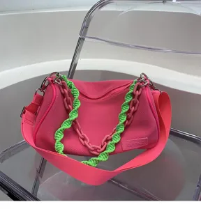 Detail view of pink canvas shoulder bag with neon green chain strap, modern niche design accessory.