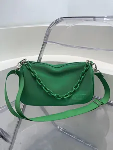 Green stylish shoulder bag with chain strap and wide webbed strap on acrylic chair
