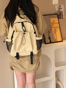 Vue détaillée d'un sac à dos beige décontracté avec plusieurs poches et cordon de serrage porté.