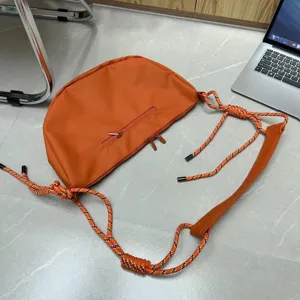 Orange nylon dumpling crossbody bag with trendy knotted climbing rope straps for casual daily use.