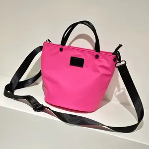 Waterproof nylon crossbody bucket bag detail, vibrant pink casual handbag with black straps.