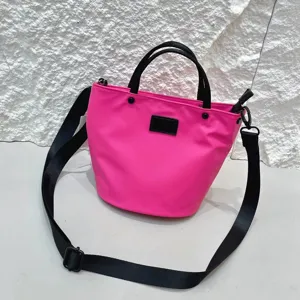 Details of pink waterproof nylon bucket bag with black handles and adjustable crossbody strap.