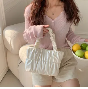 Detail view of the stylish white gathered cloud handbag held by a model with pink knit cardigan.
