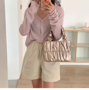 Detailed shot of stylish metallic pleated cloud handbag paired with chic cardigan and shorts.