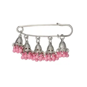 Close-up detail of silver ethnic brooch pin with hanging bell charms and pink beads decoration.