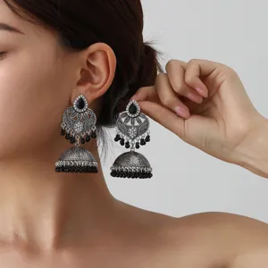 Vintage silver ethnic jhumka earrings detail shot with intricate carved patterns and black bead tassels.