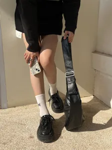Vue détaillée du sac à épaule souple en cuir noir porté avec une tenue rétro et vintage.