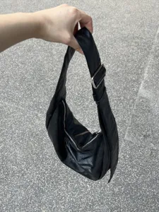 Vue détaillée du sac hobo en cuir souple noir, avec fermeture éclair et boucle en métal.