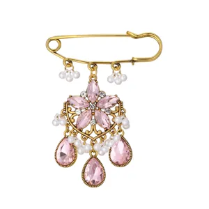 Detailed close-up of a vintage gold-toned safety pin brooch featuring pink crystal rhinestones and pearls.