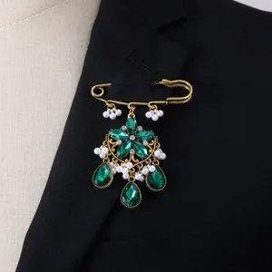 Close-up detail shot of vintage gold safety pin brooch featuring green crystals and pearls.