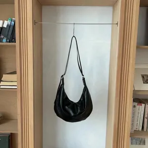 Detailed shot of a black soft leather slouchy crescent shoulder bag hanging in a chic bookshelf scene.