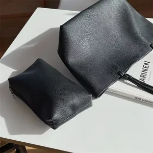Detailed view of minimalist black soft leather tote bag with matching pouch on clean white desk.