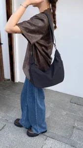 Detail view of the black nylon crescent crossbody bag worn outdoors, showing its wide strap.