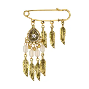 Close-up detail of vintage gold bohemian feather brooch with delicate charms and sparkling crystal.