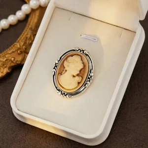 Close-up detail shot of vintage cameo brooch in white jewelry box, retro aesthetic style.