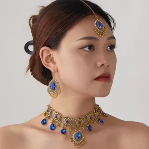 Gros plan sur collier ras du cou ethnique doré et boucles d'oreilles aux gemmes bleues.