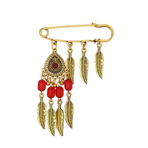 Detailed shot of vintage gold safety pin brooch with red beads and feather charms boho style