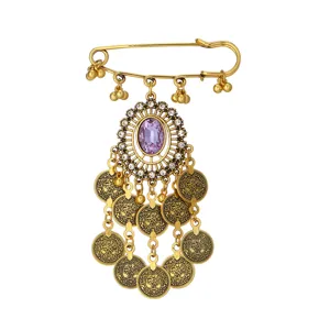 Detalle de broche bohemio vintage dorado con cristal morado y elegantes dijes de monedas.
