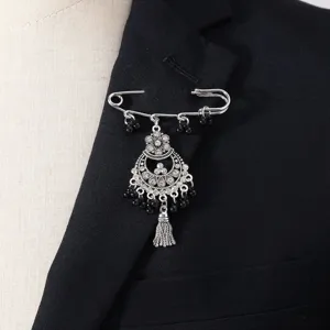 Nahaufnahme der silberfarbenen Strass-Quasten-Brosche am Revers des schwarzen Anzugs.