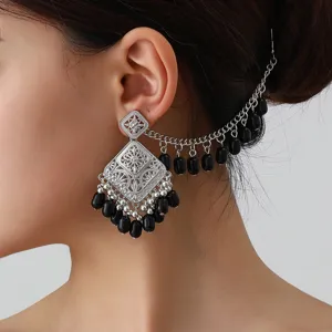 Close-up detail of ethnic vintage silver hollow earring with black beads and chain wrap.
