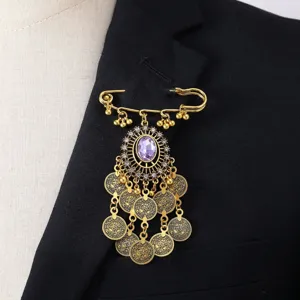 Detalle de broche estilo bohemio vintage dorado con colgantes de monedas y gran disenio.