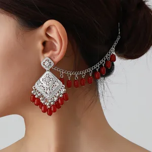 Close-up detail shot of ethnic hollow-out carved silver stud earrings with red bead tassels.