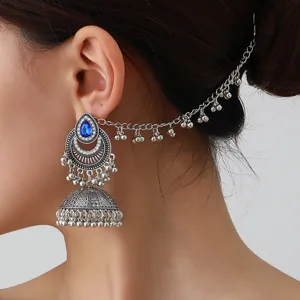 Gros plan détaillé de boucles d'oreilles bohèmes vintage argentées avec cristal bleu et chaîne.