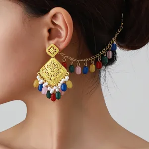 Close-up detail of ethnic hollow-carved gold earrings with colorful beads and hair chain.