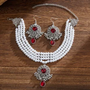 Close-up detail of vintage ethnic pearl necklace set with red gemstone pendants on wood.