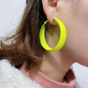Close-up detail shot of vibrant neon green painted geometric hoop earrings worn on ear.