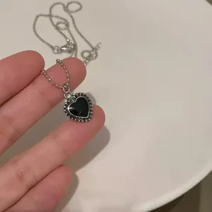 Detalle de collar con colgante de corazón negro delicado, cadena vintage y estilo chic.