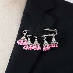 Detailed close-up shot of silver vintage bell tassel brooch with pink beads on jacket lapel.