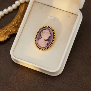 Vintage cameo brooch detailed view, elegant purple lady profile in gold tone frame.
