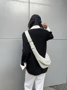 Vue détaillée d'un sac porté épaule minimaliste blanc en cuir souple porté en extérieur.