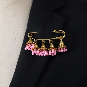 Detailed shot of retro gold safety pin brooch with pink bell tassel charms, elegant accessory.